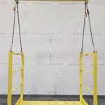 Open-end yellow material platform with overhead spreader bar and sling cables for safe hoisting of bulk equipment.